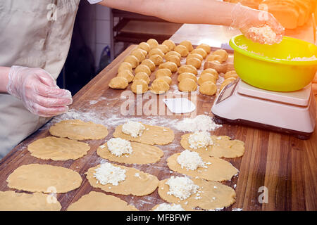 Un close-up di una femmina di baker in guanti protettivi tira fuori l'impasto per la cottura di focacce wiith formaggio su una tabella annodato con un mattarello Foto Stock