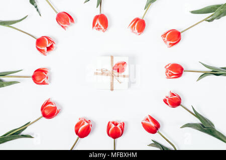 Disposizione dei tulipani rossi e un piccolo regalo al centro su un tavolo bianco vista superiore Foto Stock