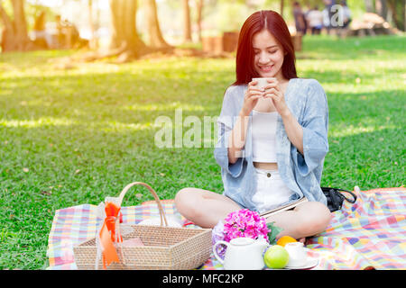 Bella donna asiatica coppa di ritegno di bere in posizione di stazionamento mentre il picnic nel parco in vacanza Foto Stock