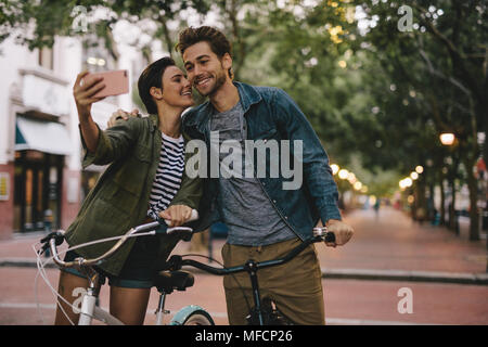 Coppia romantica con le biciclette tenendo selfie. Le donne che prendono selfie e la bacia fidanzati guancia. Foto Stock