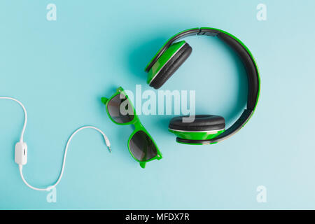 Cuffie verde e occhiali da sole con cavo isolato sul pastello blu sfondo laici piana. Foto Stock
