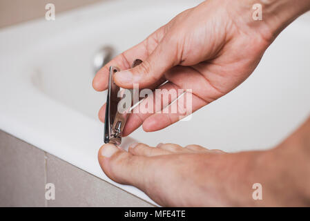 Primo piano di un giovane uomo caucasico in bagno il suo taglio toenails con un tagliaunghie Foto Stock