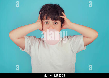 Bambino con la gomma da masticare in bocca su sfondo blu Foto Stock