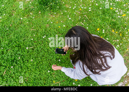 Vista dall'alto di mani di ragazza adolescente a scattare foto di fiori con il telefono cellulare. Foto Stock