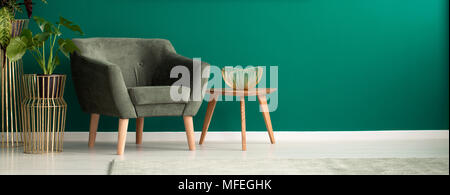 Close-up di un accogliente, scuro poltrona e un tavolo da caffè in legno in un lussuoso salotto verde interno con decorazioni dorate Foto Stock