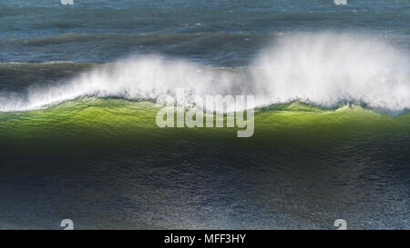 La sera tardi la luce del sole che splende attraverso una grande onda la rottura a Fistral a Newquay in Cornovaglia. Foto Stock