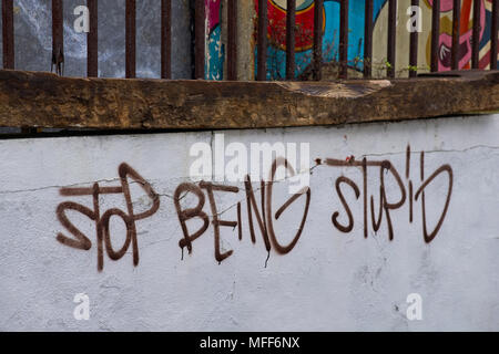 Smettere di essere stupido scritto su un muro bianco marrone con vernice spray Foto Stock