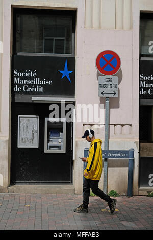 Un giovane uomo che cammina davanti a un societe Marseillaise de banca di credito Foto Stock