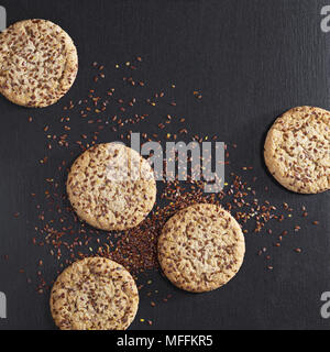 Round i cookie con sesamo e semi di lino in pietra nera di sfondo, vista dall'alto Foto Stock
