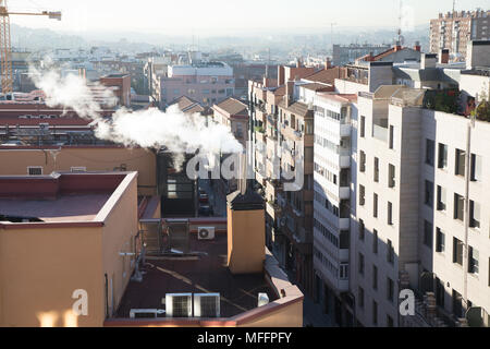 Il sollevamento di fumo dal camino di riscaldamento combustibile fossile nel tetto dell'edificio, nella città di Madrid, Spagna, Europa Foto Stock