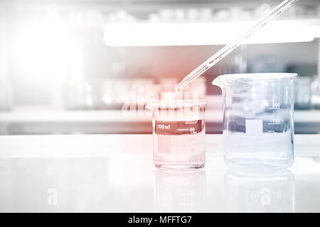 Bicchiere di vetro con acqua caduta della pipetta nell'esperimento la scienza medica lo sfondo di laboratorio Foto Stock