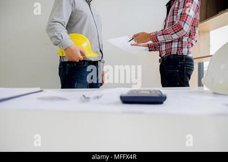 I progettisti a discutere un blueprint durante la verifica delle informazioni su un computer tablet in un ufficio. Foto Stock