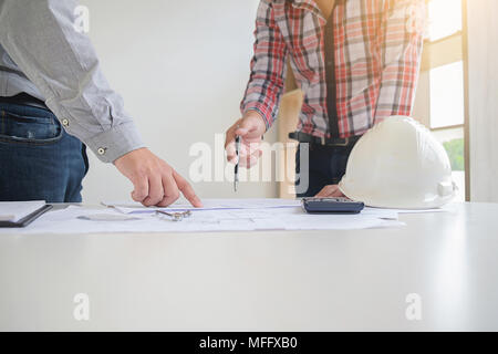 I progettisti a discutere un blueprint durante la verifica delle informazioni su un computer tablet in un ufficio. Foto Stock