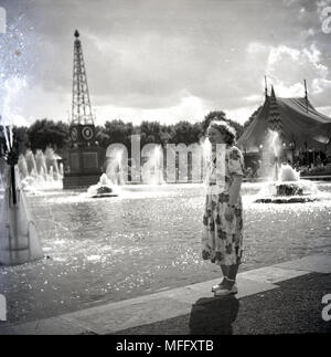 1951, storico, lady in un abito floreale in piedi da un display di acqua con fontane al Festival della Gran Bretagna, Parco di Battersea, Londra, Inghilterra, Regno Unito. L'idea dietro il festival celebra l'industria britannica, delle arti e della scienza e ispirare il pensiero di una migliore la Gran Bretagna a seguito della durezza della post-ww2 era. Foto Stock