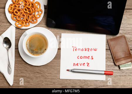 Tovagliolo proverbio del messaggio sul tavolo di legno con caffè, alcuni alimenti e tablet PC domani arriva mai Foto Stock