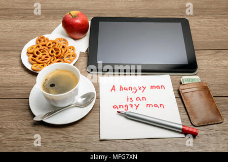 Tovagliolo scrittura proverbio del messaggio sul tavolo di legno con caffè, alcuni alimenti e tablet PC un uomo affamato è un uomo arrabbiato Foto Stock