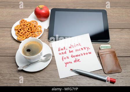 Tovagliolo scrittura proverbio del messaggio sul tavolo di legno con caffè, alcuni alimenti e tablet PC mangiare, bere e stare allegro, per domani si muore Foto Stock