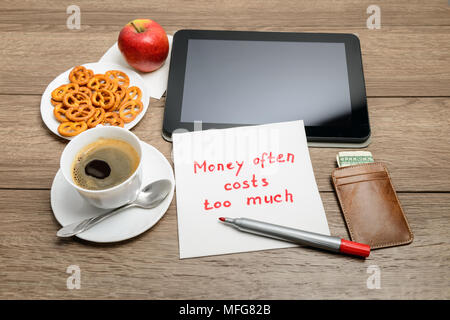 Tovagliolo scrittura proverbio del messaggio sul tavolo di legno con caffè, alcuni alimenti e tablet PC denaro spesso costa troppo Foto Stock