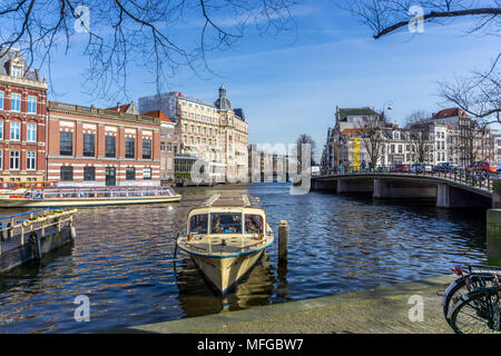 Barche sul fiume Amstel di Amsterdam, Paesi Bassi, Europa con NH Doelen Amsterdam Hotel raccolta nel backdround. Foto Stock