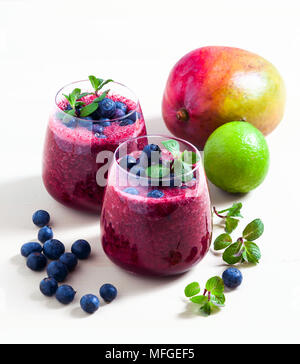 Appena sfornati i frullati di mirtilli e mango con succo di agrumi in due bicchieri. Il mangiare sano Foto Stock