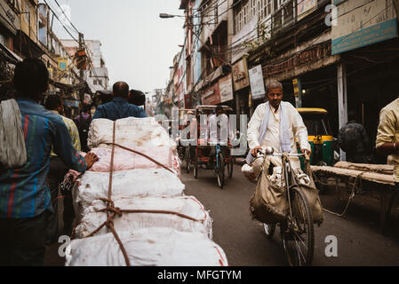 Uomo indiano sulla sua bicicletta passando uomini spingendo un carrello su una strada trafficata in Delhi durante le ore di punta Foto Stock