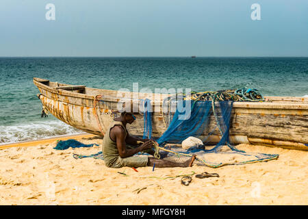L uomo che fissa le loro reti nella loro barche da pesca su una spiaggia in Robertsport, Liberia, Africa occidentale, Africa Foto Stock