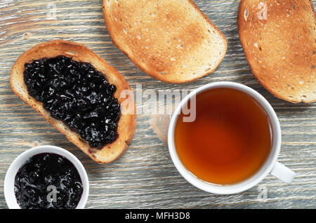Pane tostato con marmellata di mirtilli e una tazza di tè sul vecchio tavolo in legno, vista dall'alto Foto Stock