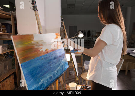 Con i capelli lunghi donna artista dipinge foto su tela con vernici a olio nella sua officina Foto Stock