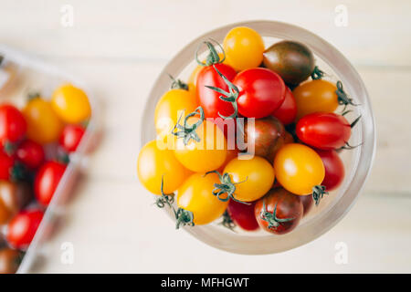 Colorate di fresco mescolato i pomodori ciliegia dentro un vasetto gass ,vista superiore, su uno sfondo bianco Foto Stock