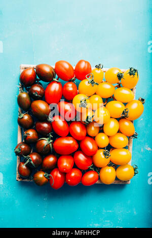 Appena lavato mescolati i pomodori ciliegia visualizzata per differenti tonalità di colore un arrugginito granito sfondo blu Foto Stock