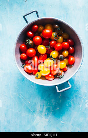 Appena lavato mescolati i pomodori ciliegia dentro uno scolapasta sopra un arrugginito granito sfondo blu Foto Stock