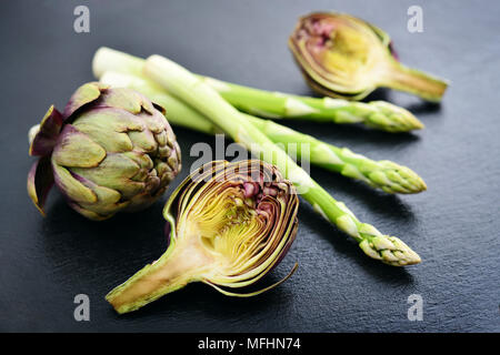 Asparagi con carciofi su nero ardesia closeup sfondo Foto Stock