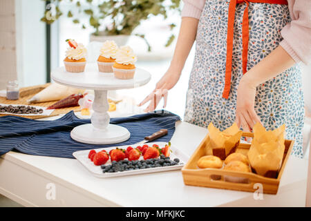 Vista ritagliata della femmina di baker come decorare le tortine, tenendo le mani sul tavolo Foto Stock
