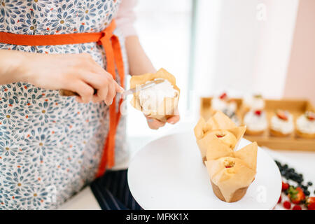 Pasticcere donna topping un tortine con crema di burro con il coltello. Tortine avvolto in carta artigianale Foto Stock