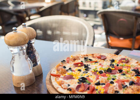 Vista ravvicinata di bel piatto pronto da mangiare. La Pizza sul tavolo nella soleggiata giornata d'estate presso la terrazza all'aperto. Ancora in vita. Foto Stock