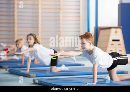 Gruppo di bambini facendo ginnastica su tappeti di blu durante l'educazione fisica classe a scuola Foto Stock