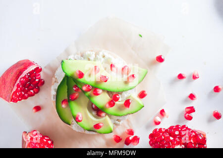 Pane croccante snack sani con fette di avocado, soft cottage cheese e i semi di melograno. Colazione semplice concetto su uno sfondo bianco con spazio di copia Foto Stock