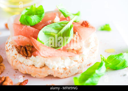 Pane croccante snack sani con prosciutto di Parma, soft cottage cheese, noci, olio d'oliva, paprica, di foglie di basilico fresco. Facile colazione close-up su una bianca bac Foto Stock