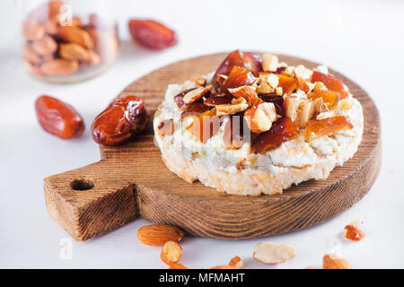 Snack sani con pane croccante, date, morbida crema di formaggio, mandorle e noci. Facile colazione close-up su uno sfondo bianco con copia spazio. Foto Stock