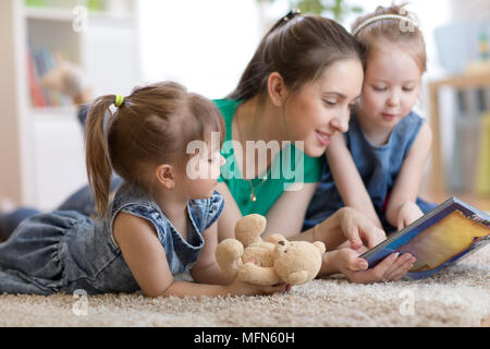 Giovane mamma e i suoi figli sdraiato sul pavimento e libro di lettura Foto Stock