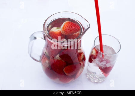 Fragola drink in una brocca e un bicchiere di bibita con cubetti di ghiaccio e una cannuccia. Foto Stock