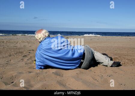 Senior man aventi un pisolino sul Portobello Beach, Edimburgo, Scozia. Regno Unito. Data: 12.01.2006 Ref: B343 093051 0002 COMPU Foto Stock