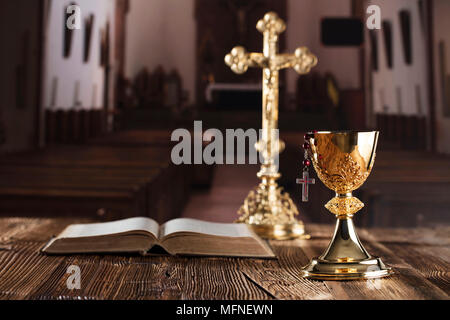 Prima Santa Comunione tema. La Croce, la Sacra Bibbia, rosario e Calice d oro su sfondo marrone. Foto Stock