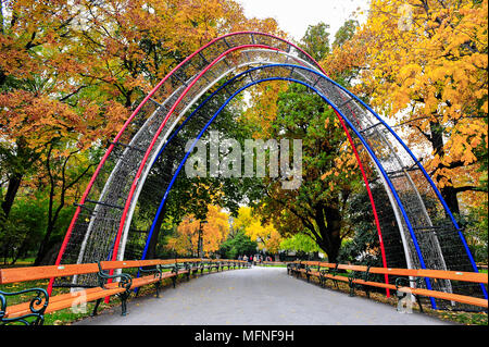 Il rosso e il blu ingresso ad arco, una colorata orlate da alberi avenue, e lunghi filari di panchine. In autunno, Stadtpark Vienna. Foto Stock
