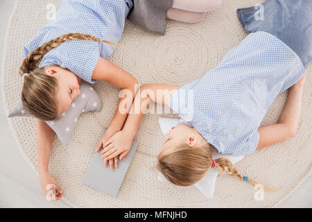 Vista dall'alto di giovani figlie gemelle giacente su un tappeto di vimini, tenendo le mani, parlando di problemi e di supporto di ciascun altro Foto Stock