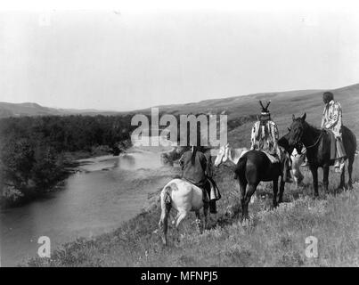 Tre Piegan indiani e quattro cavalli sulla collina sopra il fiume, 1910. Fotografia di Edward Curtis (1868-1952). Foto Stock