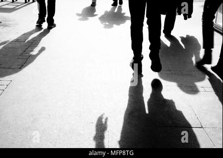 I contorni e le ombre delle persone che camminano sul marciapiede della città in mattina presto in bianco e nero Foto Stock