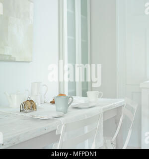 Dettaglio di un moderno paese in stile sala da pranzo, bianco tavolo in legno con teacups, pitturato di bianco sedie in metallo Foto Stock