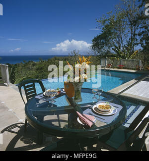 Un esterno di tavolo da pranzo con due posto l'impostazione di una terrazza solarium e una piscina esterna con un paesaggio costiero in background. Foto Stock