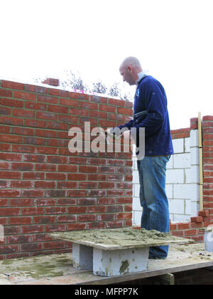 Builder / lavoratore edile la costruzione di un muro di mattoni mattoni di cementazione in su una estensione o la nuova proprietà modello di rilascio Foto Stock